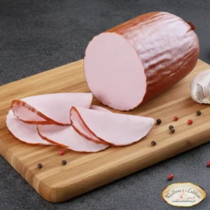 Wędzona mortadela w kawałku i plastrach na drewnianej desce obok ząbków czosnku i ziaren pieprzu.